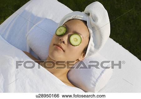 Stock Photograph - Young woman with cucumbers over eyes, lying on massage table outdoors. Fotosearch