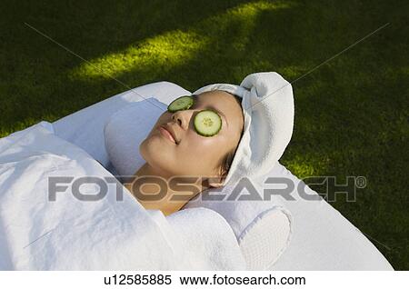Stock Photography - Young woman with cucumbers over eyes, lying on massage table outdoors. Fotosearch