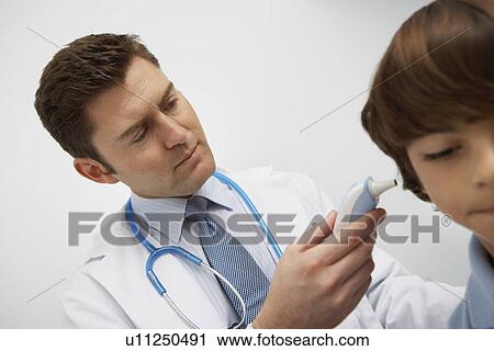 Stock Image - Boy having temperature taken with ear thermometer. Fotosearch