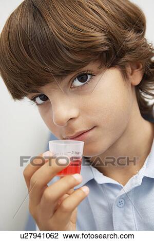 Stock Image - Boy holding medicine in liquid measure, portrait. Fotosearch