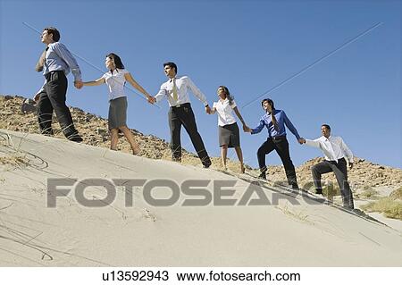 Business people holding hands while walking uphill in the desert. View Large Photo Image Stock Image - Business people holding hands while walking uphill in the desert.. Fotosearch