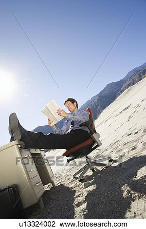 Stock Image - Businessman Sitting At Desk in the Desert. Fotosearch