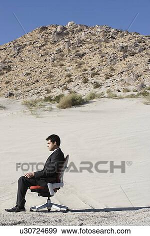 Stock Photo - Businessman Sitting on Chair in the Desert. Fotosearch