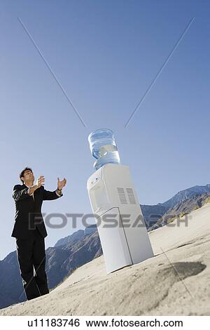 Businessman Standing by Water Cooler in the Desert View Large Photo Image Stock Photograph - Businessman Standing by Water Cooler in the Desert. Fotosearch