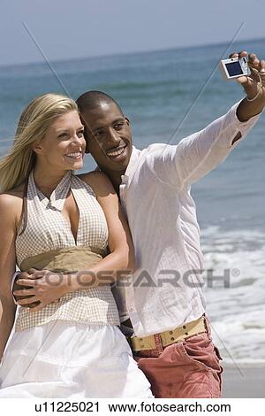 Stock Image - Couple taking photo on beach. Fotosearch