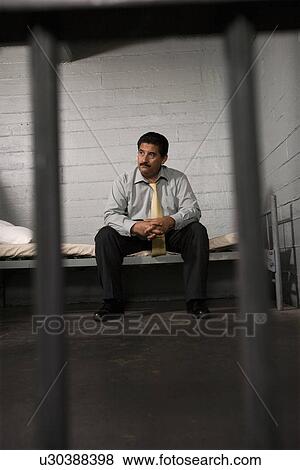 Stock Photo - Criminal sitting on bed in jail. Fotosearch