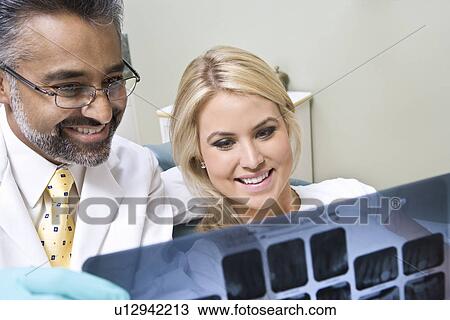 Stock Image - Dentist and patient looking at x-ray. Fotosearch