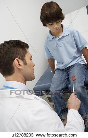 Stock Image - Doctor examining boy with reflex hammer. Fotosearch