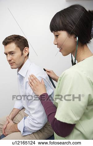 Picture - Doctor examining male patient using stethoscope in hospital. Fotosearch