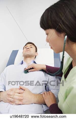 Stock Image - Doctor examining male patient using stethoscope in hospital. Fotosearch