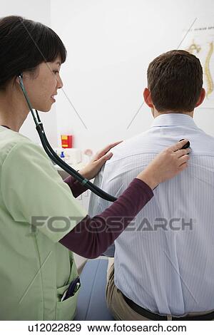 Doctor examining male patient using stethoscope in hospital View Large Photo Image Stock Photo - Doctor examining male patient using stethoscope in hospital. Fotosearch