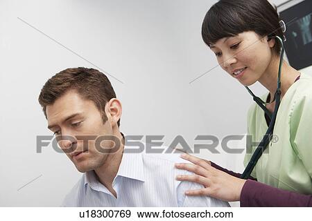 Stock Photo - Doctor examining male patient using stethoscope in hospital. Fotosearch