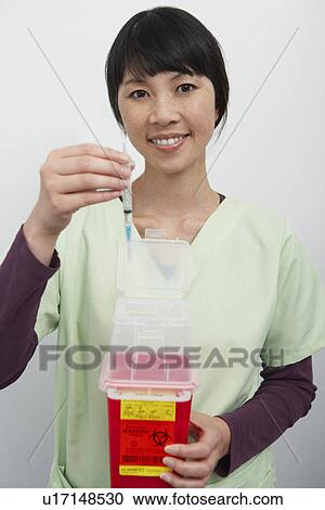 Stock Image - Doctor holding hyperdermic needles in hospital, portrait. Fotosearch