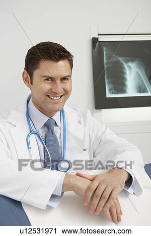 Stock Image - Doctor wearing earpiece in hospital, portrait. Fotosearch