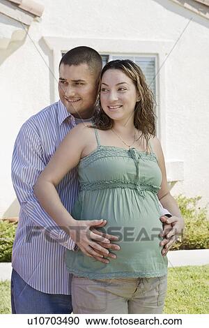 Stock Image - Expectant couple embracing outdoors. Fotosearch