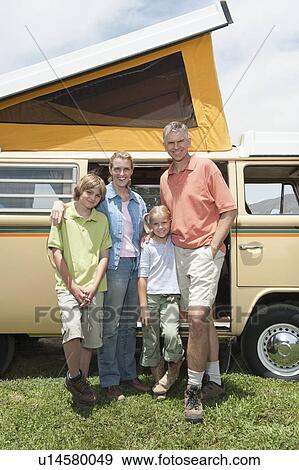 Stock Photo - Family of four stand at campervan. Fotosearch