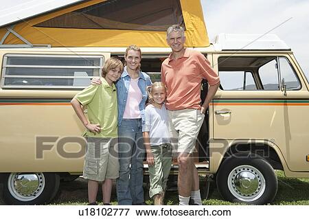 Stock Photo - Family of four stand at campervan. Fotosearch