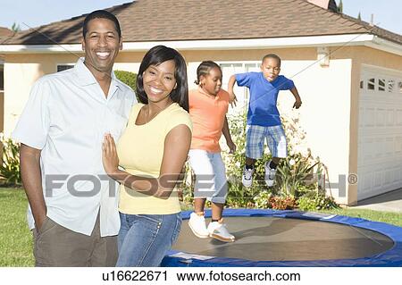 Stock Image - Family outside house, children on trampoline. Fotosearch