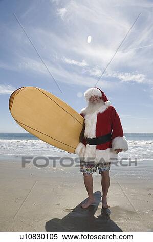 Father Christmas stands with a surfboard at the beach View Large Photo Image Stock Photography - Father Christmas stands with a surfboard at the beach. Fotosearch