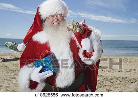 Stock Photograph - Father Christmas stands with his sack on a beach. Fotosearch