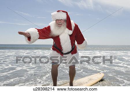 Picture - Father Christmas surfboards at the waters edge. Fotosearch