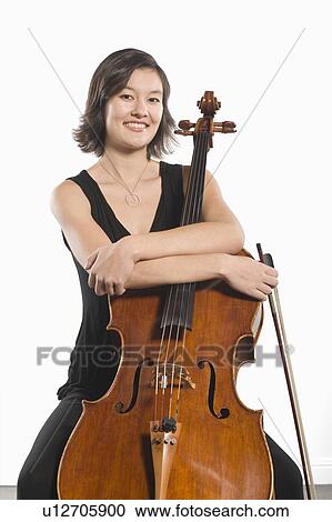 Stock Image - Female cellist sits with arms folded across cello. Fotosearch