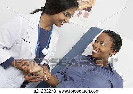 Stock Image - Female doctor checking patient's pulse. Fotosearch
