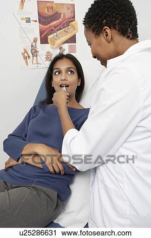 Stock Image - Female doctor examining patient's throat. Fotosearch