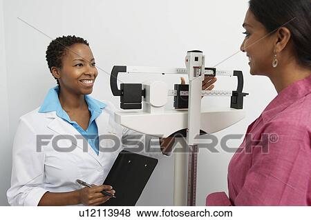 Stock Photo - Female doctor weighing patient. Fotosearch