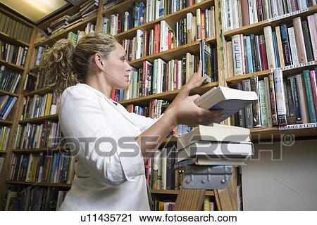 Female librarian putting books on shelves View Large Photo Image Stock Image - Female librarian putting books on shelves. Fotosearch