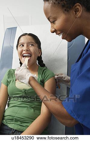 Stock Image - Female nurse checking girls tongue in hospital. Fotosearch