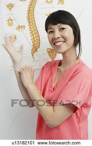 Stock Image - Female nurse putting on gloves in hospital, portrait. Fotosearch