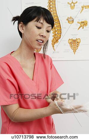 Stock Photo - Female nurse putting on gloves in hospital. Fotosearch