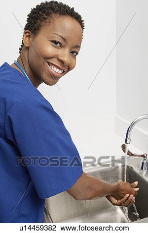 Stock Image - Female nurse washing hands in hospital, portrait. Fotosearch