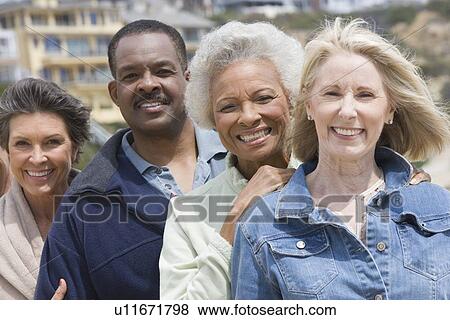 Stock Photo - Four senior adults stand in a row smiling at camera. Fotosearch