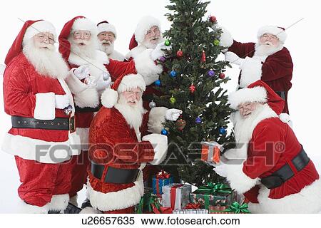 Stock Photography - Group of men dressed as Santa Claus decorating Christmas tree. Fotosearch