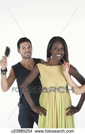 Picture - hair stylist stands behind model in yellow dress with hairbrush. Fotosearch