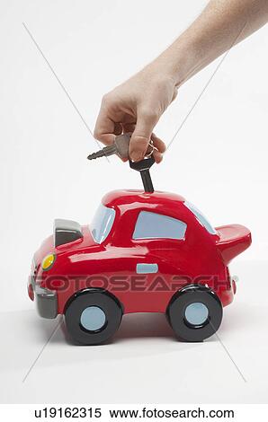 Stock Photography - Hand Putting Car Keys in Car Shaped Piggy Bank. Fotosearch