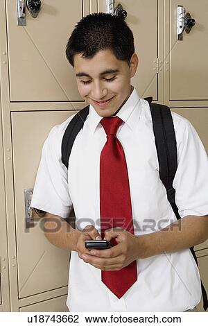 Stock Image - High School Boy Text Messaging by School Lockers. Fotosearch