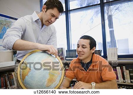 Stock Image - High School Teacher Pointing out Location on Globe to Student. Fotosearch