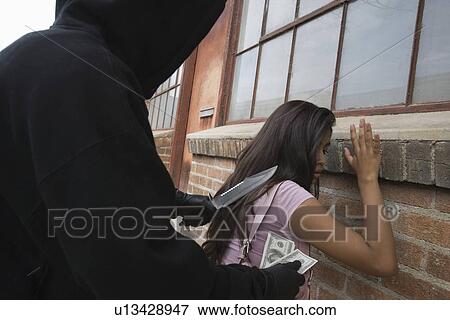 Stock Photo - Hooded man robbing young woman with knife. Fotosearch
