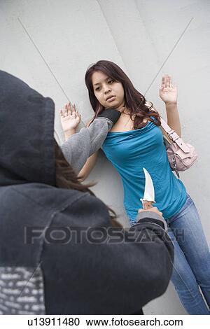Stock Image - Hooded woman robbing young woman with knife. Fotosearch