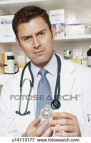 Stock Photo - Male doctor holding medication bottle in hospital, portrait. Fotosearch