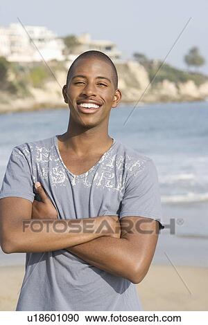 Stock Image - Man on beach, arms folded, smiling. Fotosearch