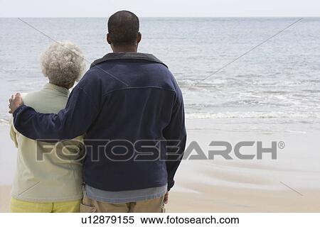 Stock Photography - Man stands with his arm round a woman at waters edge. Fotosearch