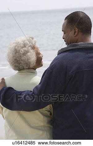 Stock Photography - Man stands with his arm round a woman at waters edge. Fotosearch