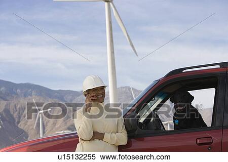 Stock Photography - Mature woman by truck at wind farm. Fotosearch