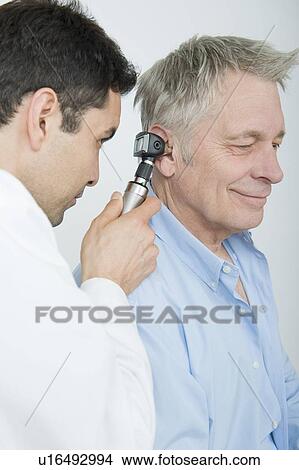 Mid adult doctor checks hearing of senior patient View Large Photo Image Picture - Mid adult doctor checks hearing of senior patient. Fotosearch