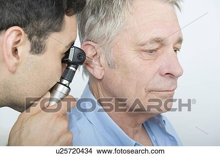 Picture - Mid adult doctor checks hearing of senior patient. Fotosearch