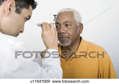 Stock Photo - Mid adult doctor examines senior man's eyesight. Fotosearch